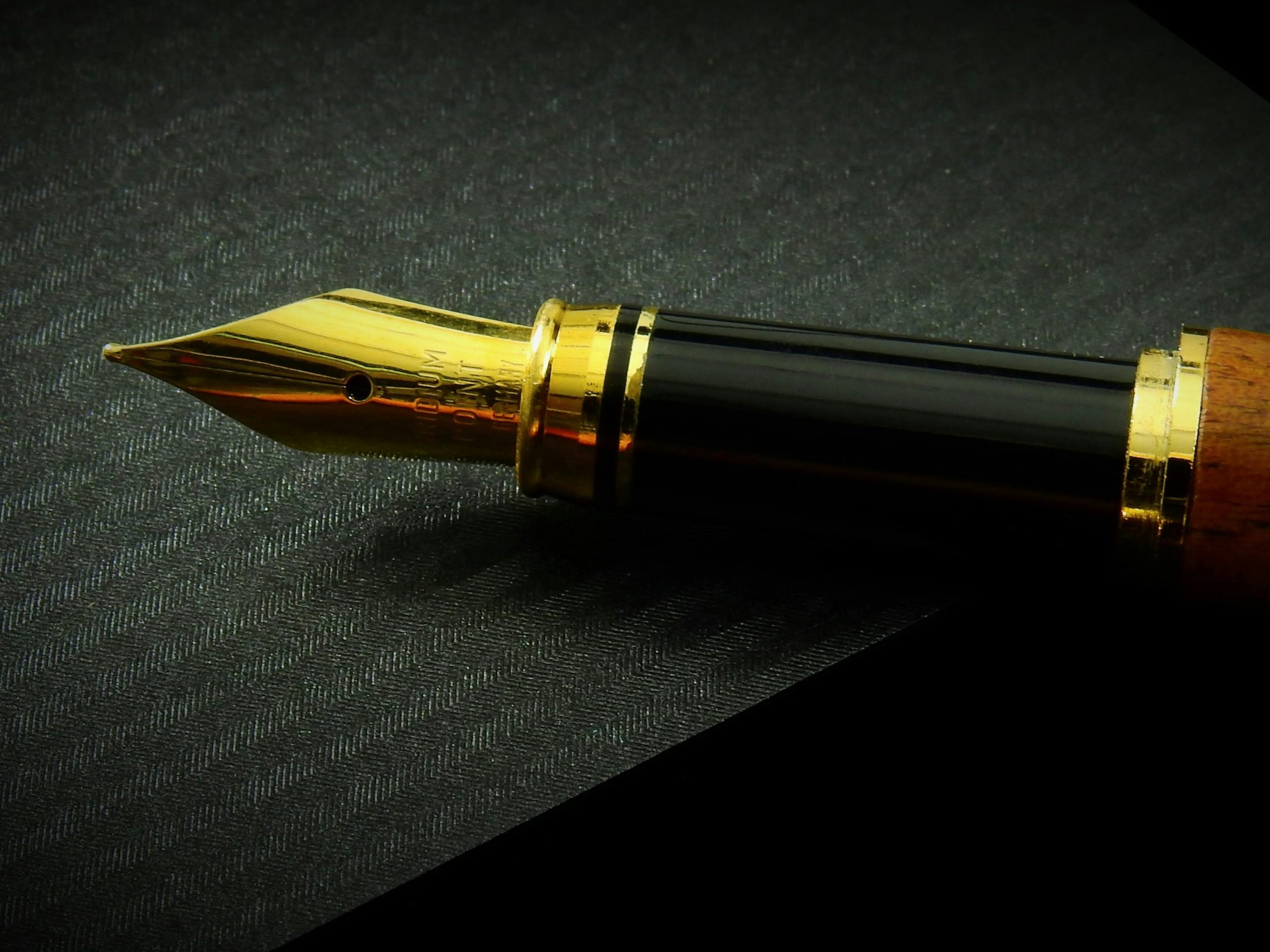 Detailed close-up of a classic fountain pen nib on textured black paper, showcasing elegance.